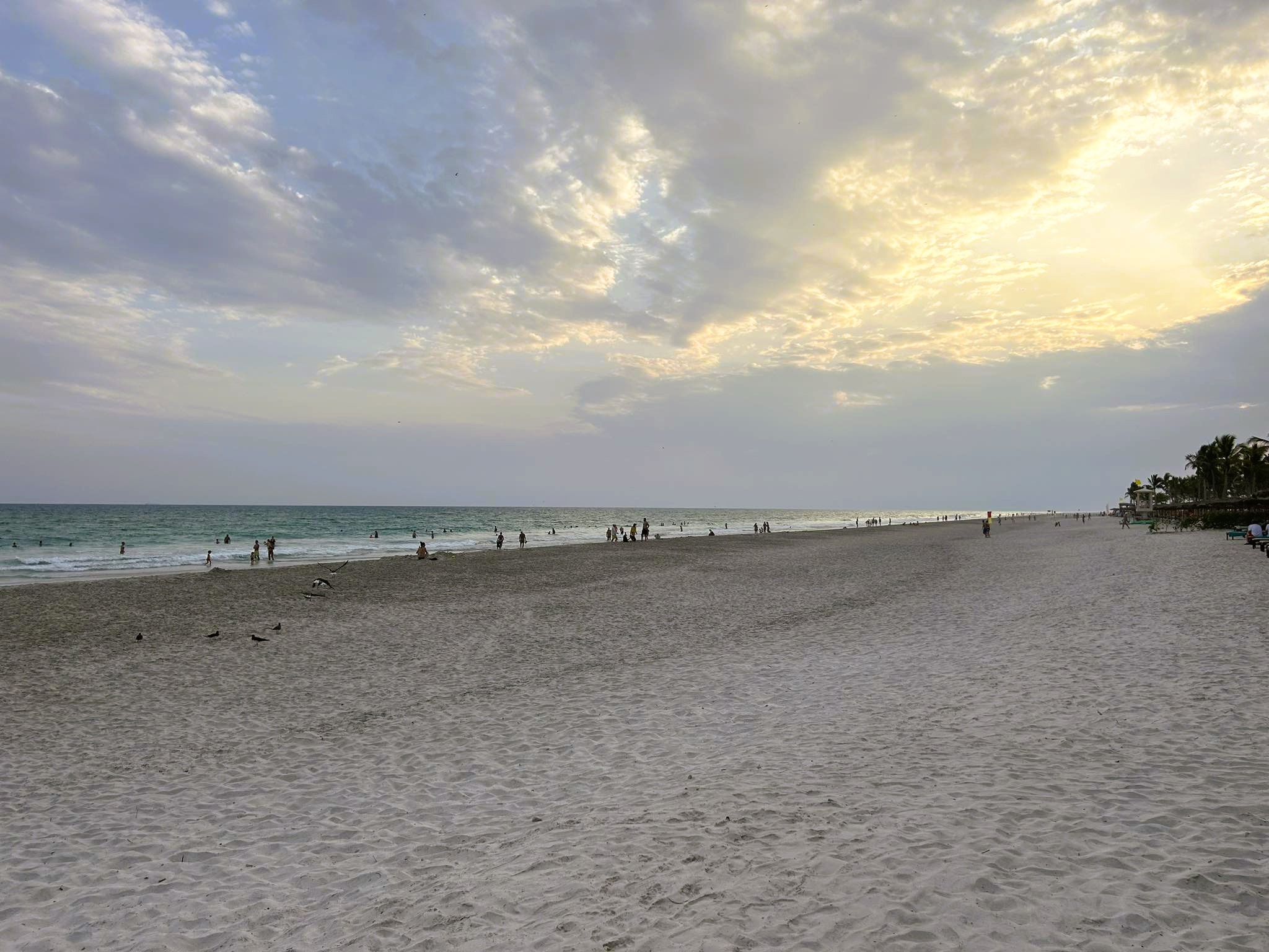 Beautiful sunset over the Salalah beach, with people walking along the shore.