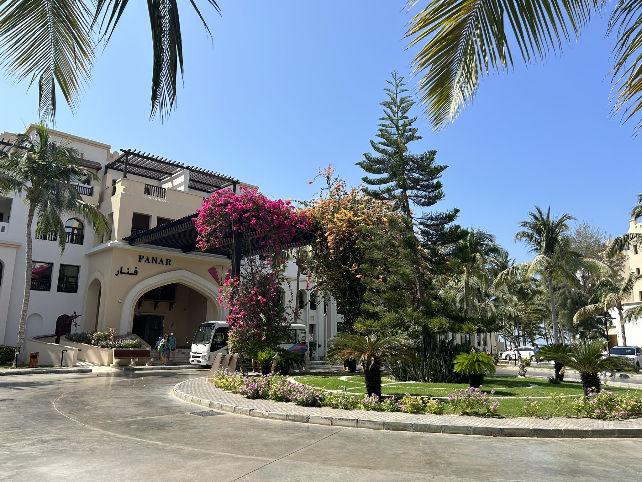 Elegant entrance of Fanar Hotel Salalah, surrounded by lush greenery and palm trees.