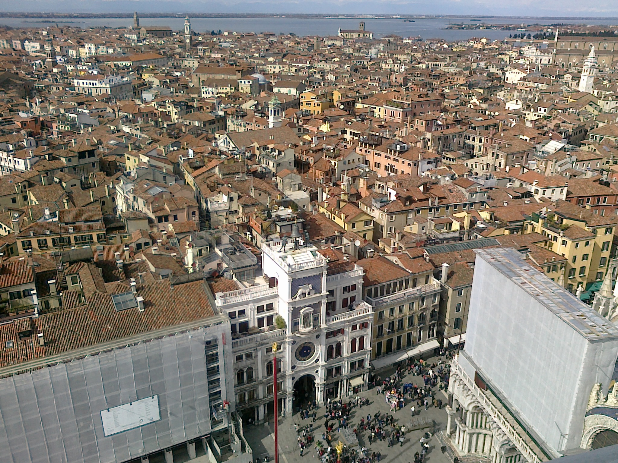 A bird's eye view of a Venetian square with a crowd of people and a distinctive clock tower.