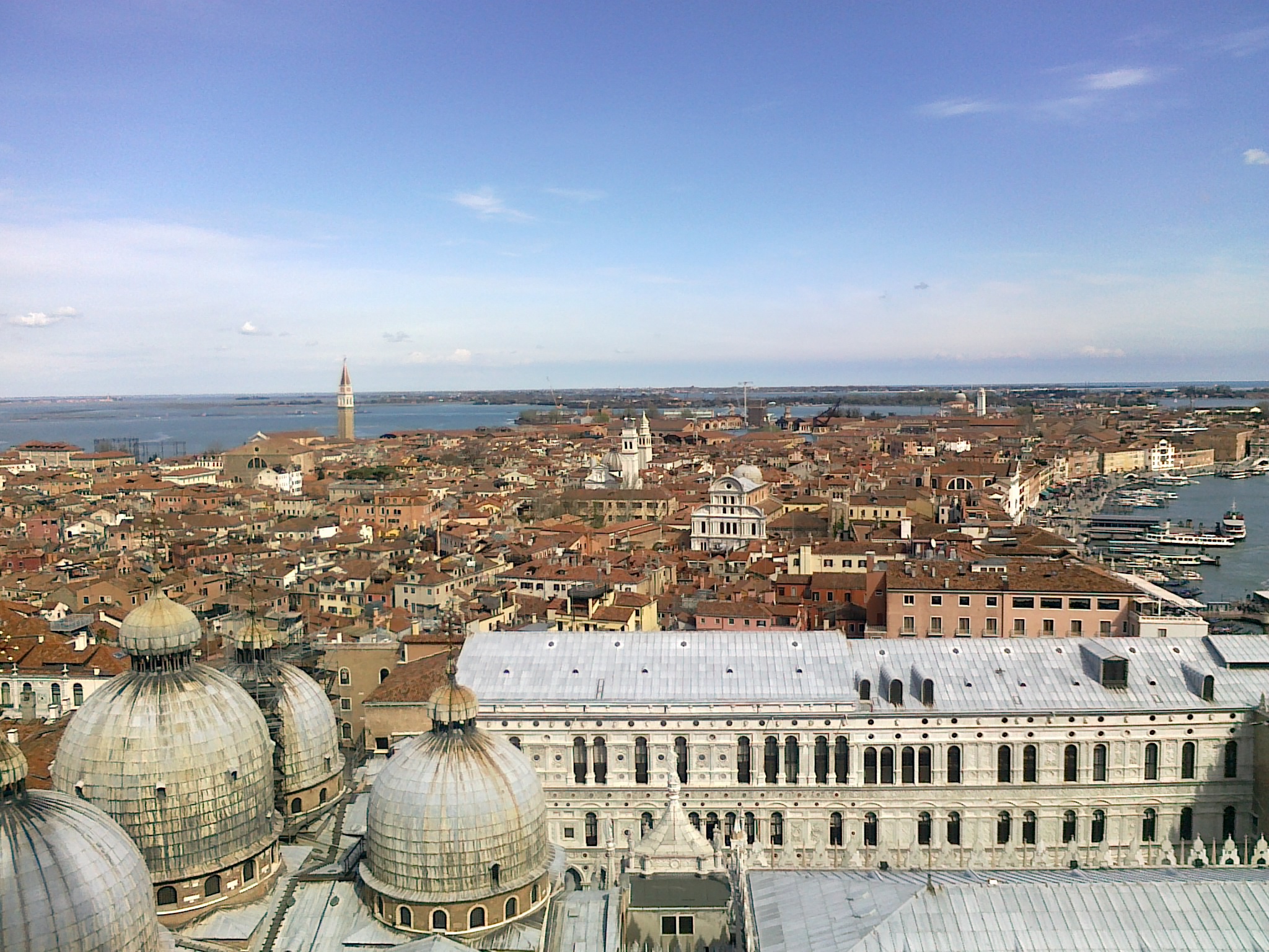 An aerial view of Venice's cityscape with numerous red rooftops and a distant view of the sea.