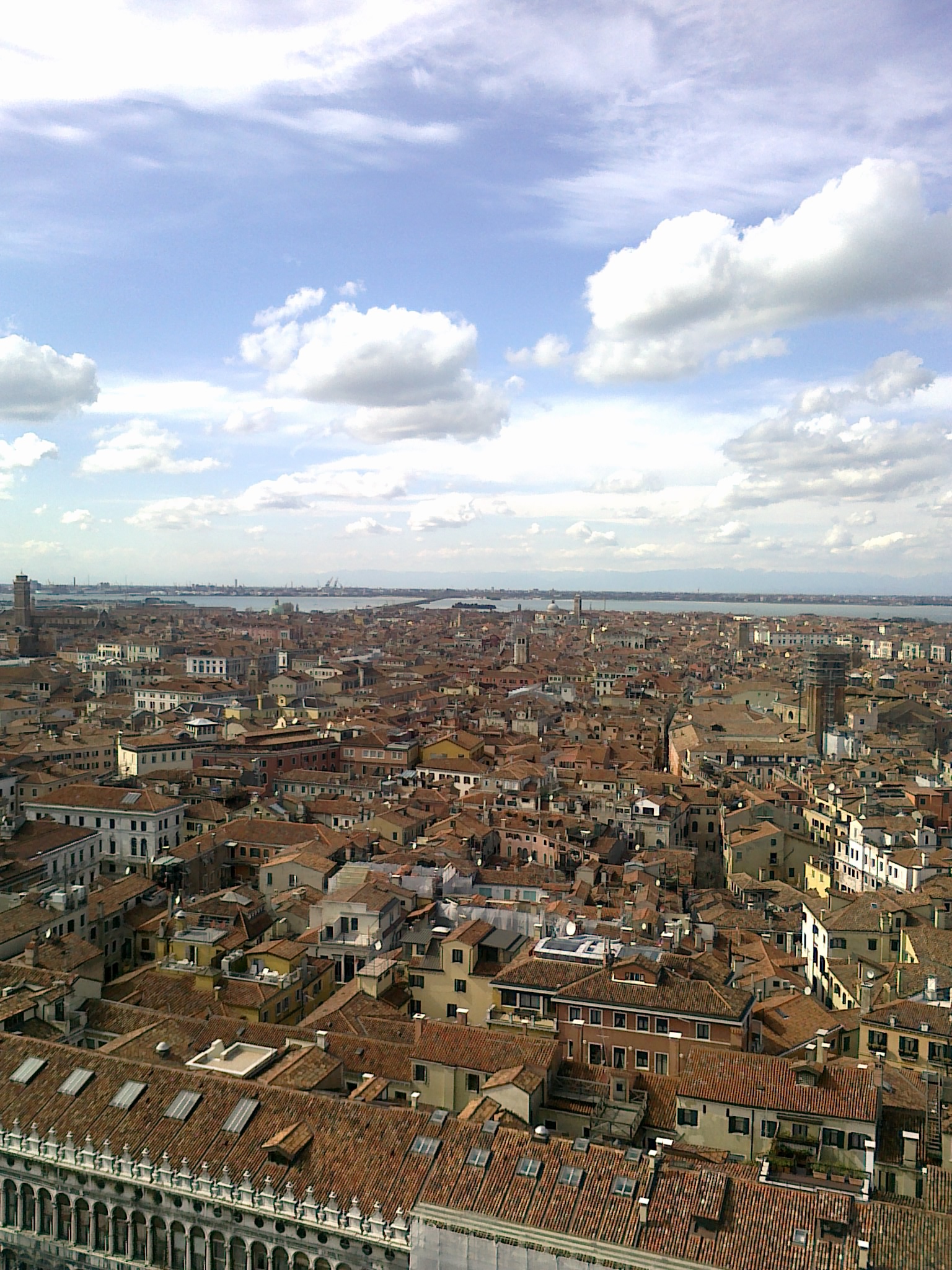 A wide aerial view of Venice showing the dense buildings and a large body of water on the horizon.